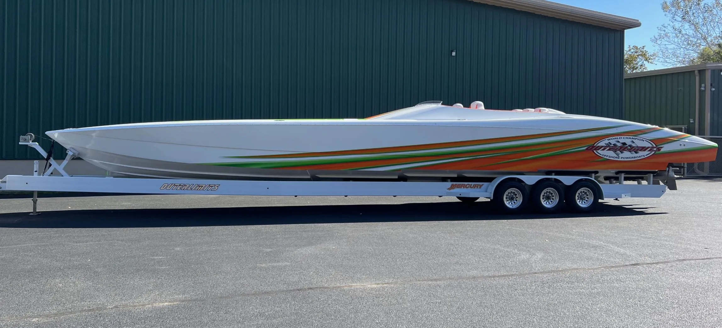 2015 Outerlimits SL-50 speedboat on a trailer, parked outside a green building.