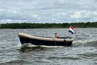 Interboat 21 Classic motorboat cruising on a lake, displaying a flag, under cloudy skies.