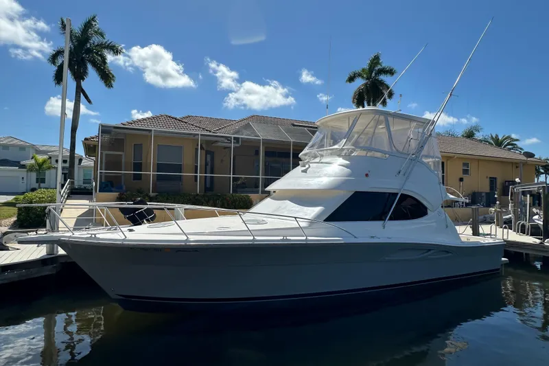 Game On Yacht Photos Pics 2002 Riviera 40 Flybridge yacht docked by a waterfront home under a clear blue sky.