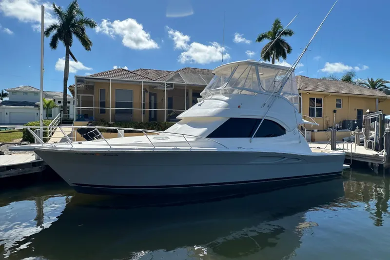 Game On Yacht Photos Pics 2002 Riviera 40 Flybridge yacht docked by a waterfront home with palm trees.