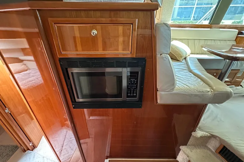Game On Yacht Photos Pics 2002 Riviera 40 Flybridge interior with microwave, wooden cabinetry, and cushioned seating area.