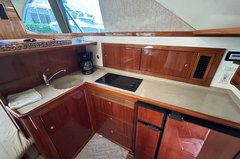 Game On Yacht Photos Pics 2002 Riviera 40 Flybridge yacht kitchen with wood cabinetry, sink, stove, and mini fridge.