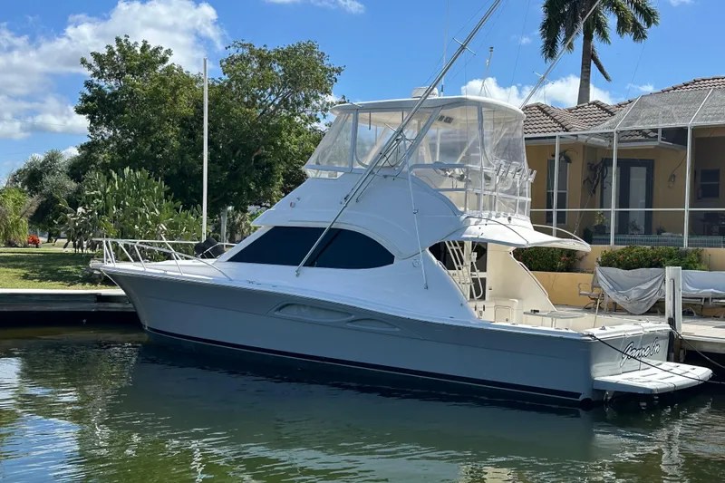 Game On Yacht Photos Pics 2002 Riviera 40 Flybridge yacht docked by a waterfront home.