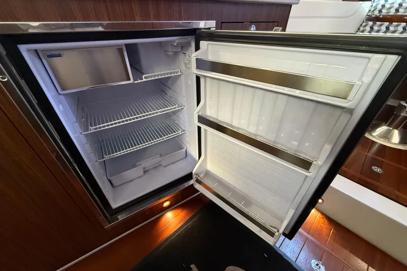 Bon Voyage Yacht Photos Pics Open refrigerator inside 2019 Pursuit OS 355 Offshore boat, showcasing interior shelves.
