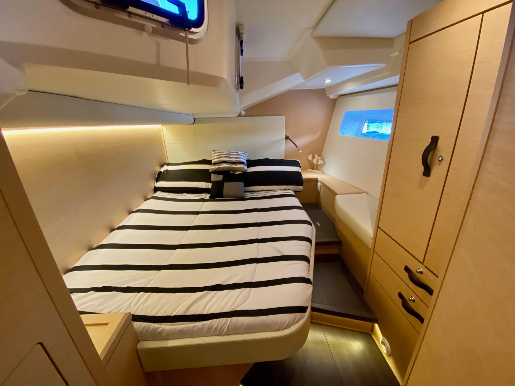 Luxurious cabin interior of 2016 Jeanneau 54 yacht with striped bedding and modern wood finish.