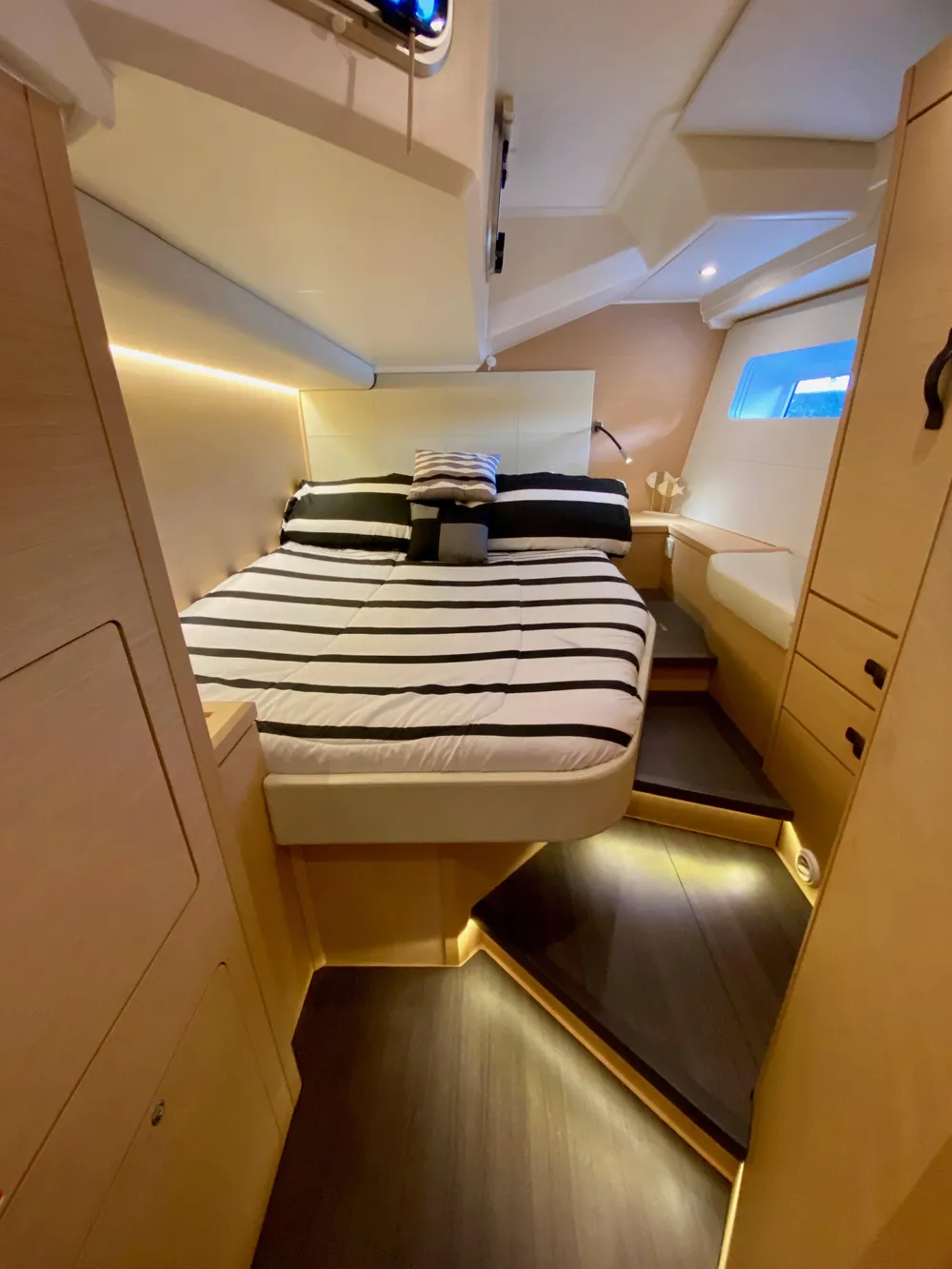 Luxurious cabin interior of 2016 Jeanneau 54 yacht with striped bedding and ambient lighting.