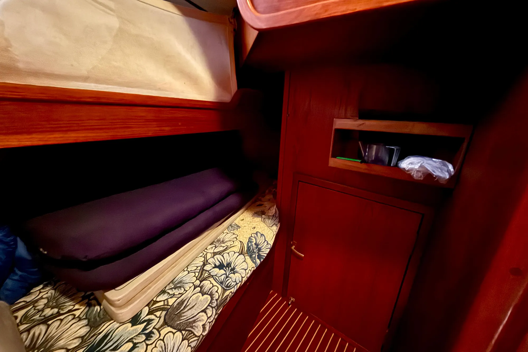 Cozy cabin interior of 1986 Nauticat 43 sailboat with wooden furnishings and floral bedding.