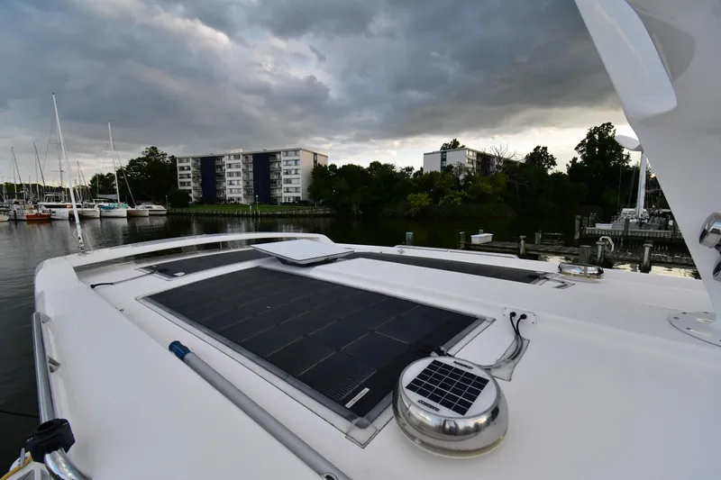 Promesa Yacht Photos Pics Hylas M44 yacht with solar panel, docked near modern buildings, under cloudy sky.