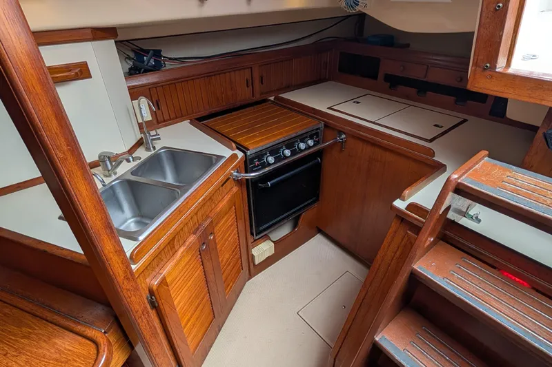 Lone Star Yacht Photos Pics 1988 Island Packet 38 yacht kitchen with wooden cabinetry, dual sink, and stove.