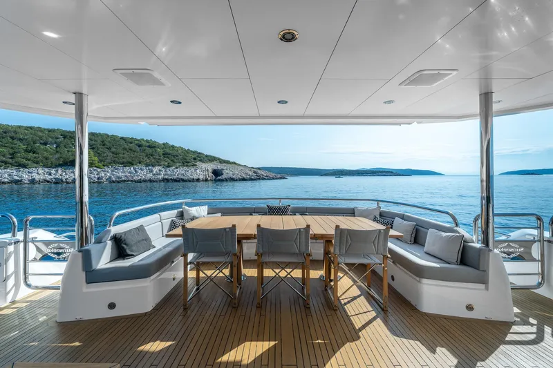 Noroader Yacht Photos Pics Luxury Sunseeker 116 yacht deck with dining area, overlooking serene ocean and coastal landscape.
