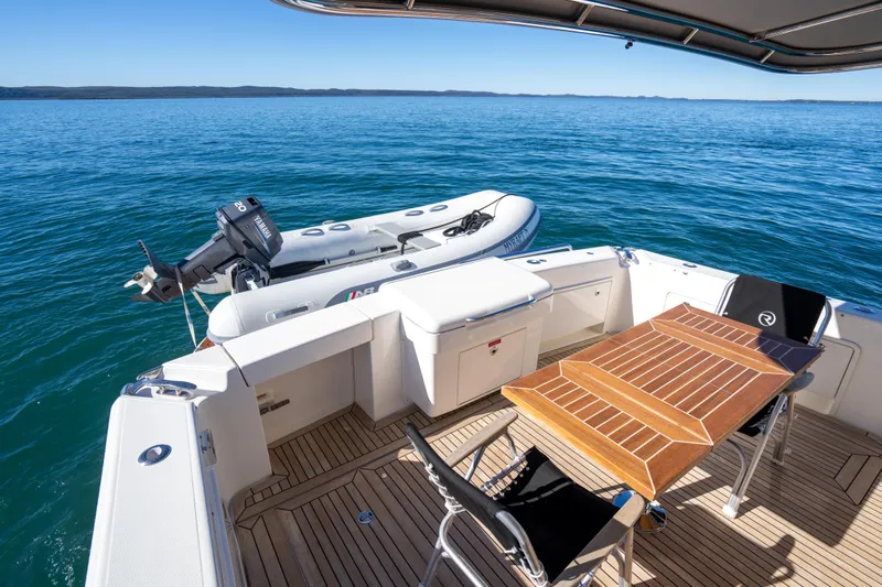  Yacht Photos Pics 2022 Riviera 445 SUV yacht deck with table, chairs, and inflatable boat on calm water.