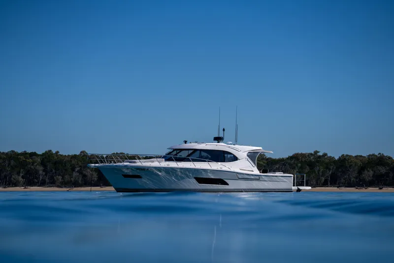  Yacht Photos Pics 2022 Riviera 445 SUV yacht on calm water with forested shoreline background.