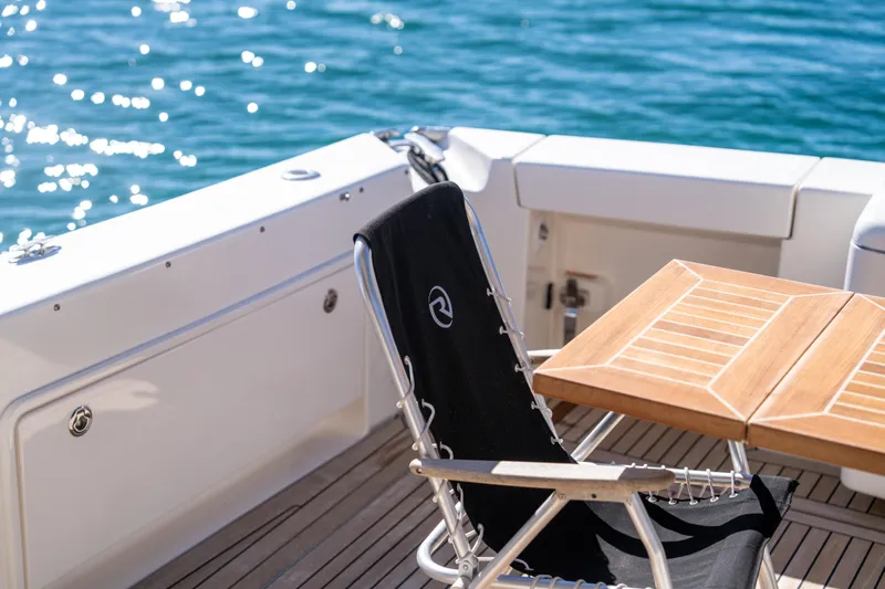  Yacht Photos Pics Deck of 2022 Riviera 445 SUV with chair and table, overlooking sparkling water.