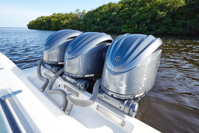  Yacht Photos Pics Triple Yamaha outboard engines on a 2022 Contender 35 ST boat, near lush shoreline.