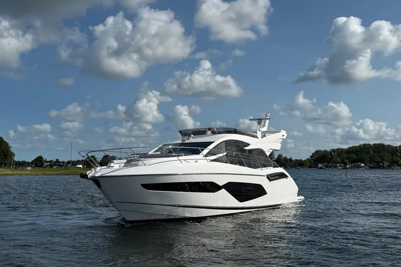 Yacht Photos Pics 2024 Sunseeker Manhattan 55 yacht cruising on a serene waterway under a partly cloudy sky.
