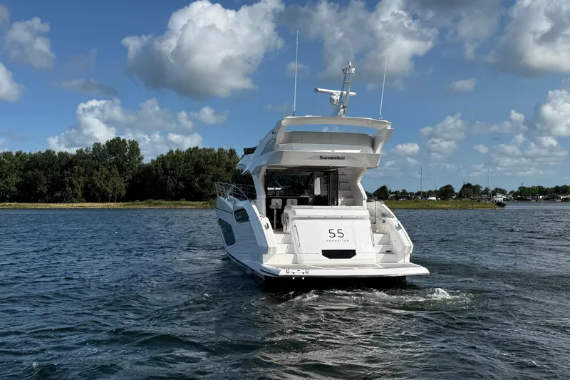  Yacht Photos Pics 2024 Sunseeker Manhattan 55 yacht cruising on a scenic waterway under a blue sky.