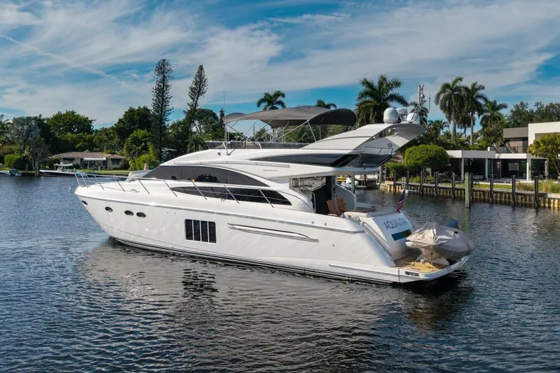 Aquavita Yacht Photos Pics 2012 Princess 64 Flybridge Motor Yacht on a serene waterway, surrounded by lush greenery.