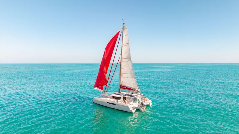 Encantado Yacht Photos Pics Sailing catamaran NEEL 47, 2023 model, with red sail on turquoise sea.