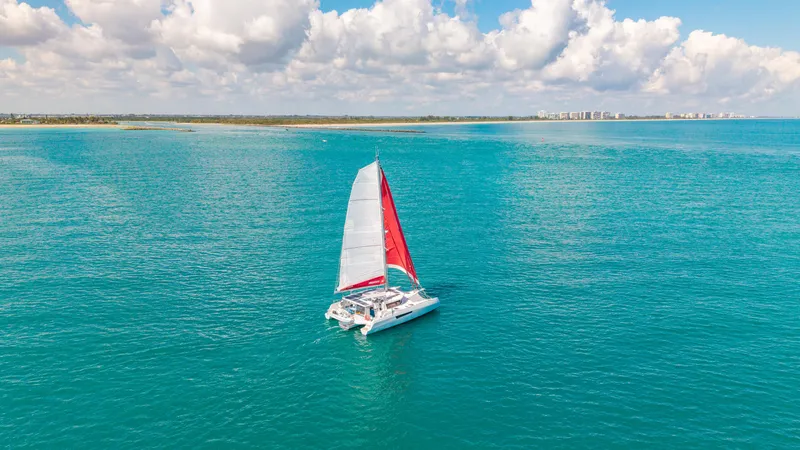 Encantado Yacht Photos Pics Sailing catamaran NEEL 47 on turquoise ocean, 2023 model, under a partly cloudy sky.