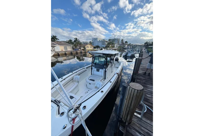  Yacht Photos Pics 2021 Wellcraft 302 Fisherman boat docked by a scenic waterfront under a blue sky.