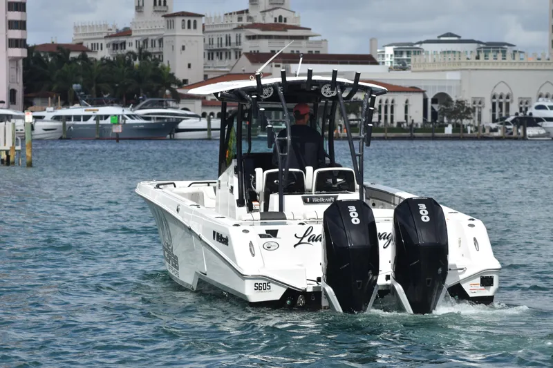  Yacht Photos Pics 2021 Wellcraft 302 Scarab boat cruising in a marina with luxury yachts in the background.