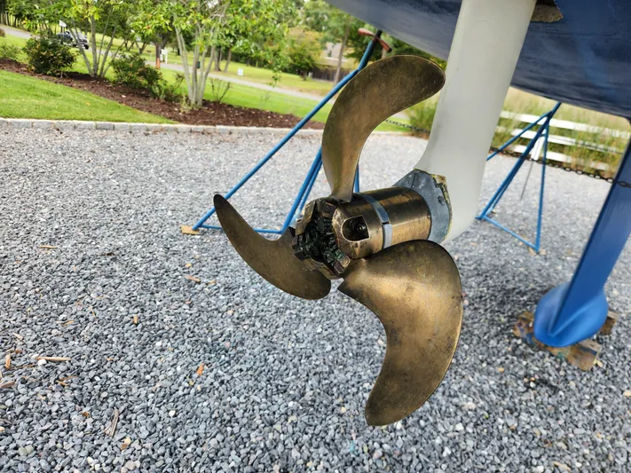 Ceres Yacht Photos Pics Propeller of 2016 Hallberg-Rassy 342 sailboat on gravel, with green foliage background.