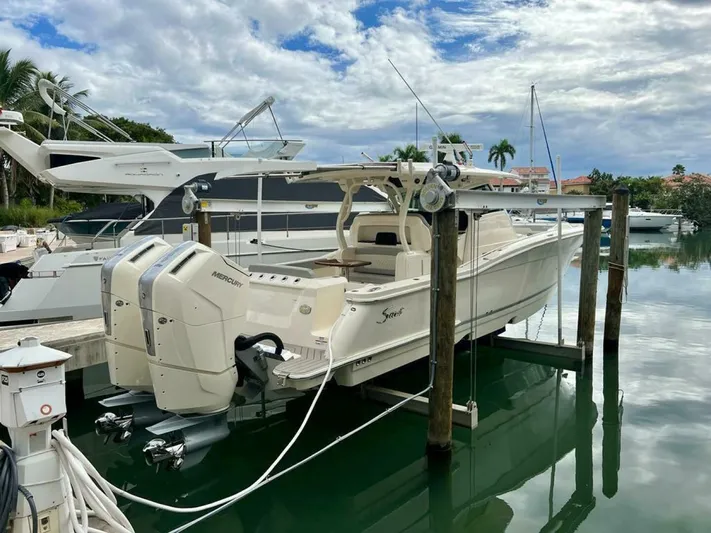  Yacht Photos Pics 2023 Scout 377 LXF boat docked with twin Mercury engines, under a partly cloudy sky.