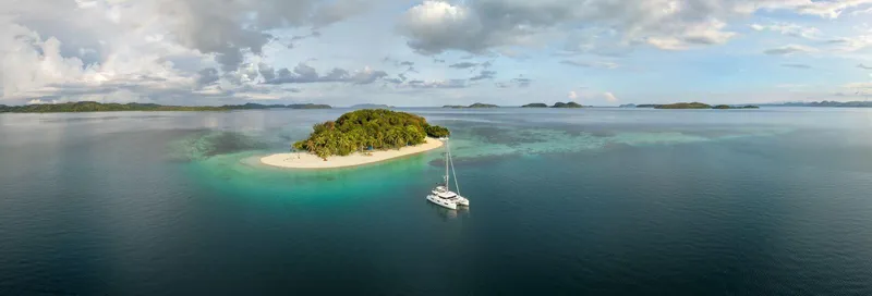 Blossom Yacht Photos Pics Aerial view of Lagoon 46 catamaran near a tropical island, 2024 model.