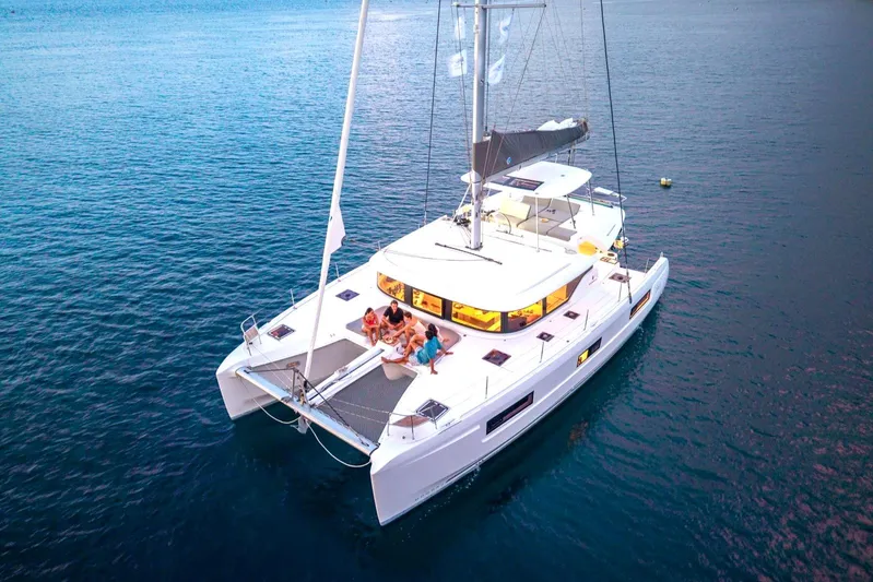 Blossom Yacht Photos Pics 2024 Lagoon 46 catamaran sailing on calm blue waters with people relaxing on deck.