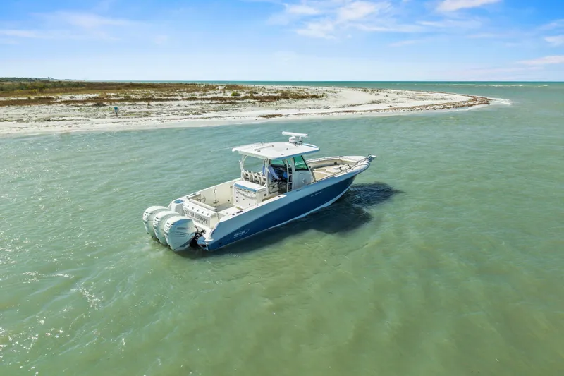  Yacht Photos Pics 2017 Boston Whaler 350 Outrage boat cruising near a sandy shoreline under a clear blue sky.