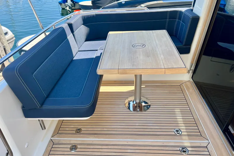 Kala Yacht Photos Pics Luxurious seating area on a 2018 Nimbus 365 Coupe yacht with wooden table and blue cushions.