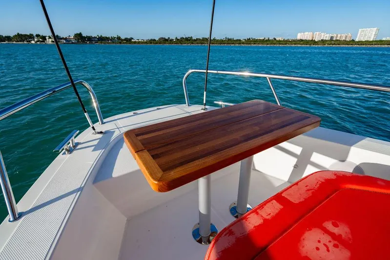 Volare Yacht Photos Pics 2023 Nimbus T11 boat deck with wooden table and red seating, overlooking calm blue waters.