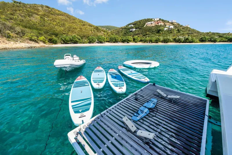 C Sisters Yacht Photos Pics 2023 Bali 5.4 Catamaran with paddleboards and inflatable in turquoise waters near lush island.