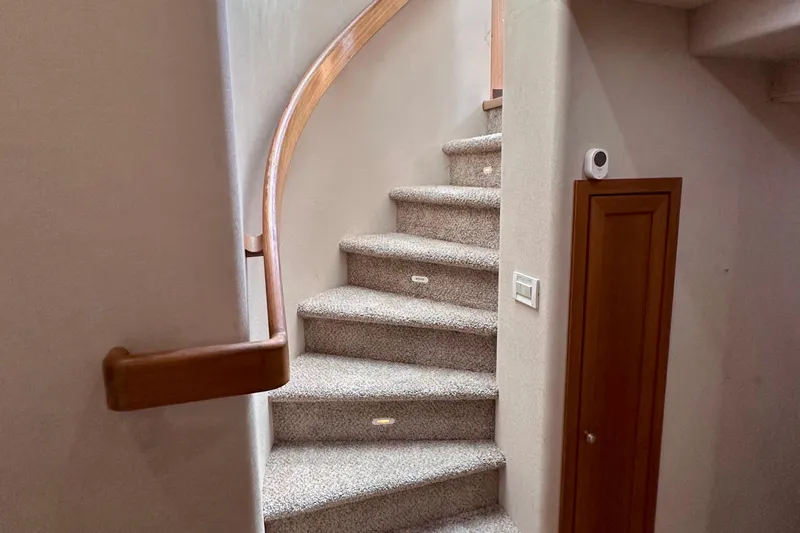 Chasing Sunsets Yacht Photos Pics Curved staircase inside 2000 Pacific Mariner 65 Motoryacht, featuring carpeted steps and wooden handrail.