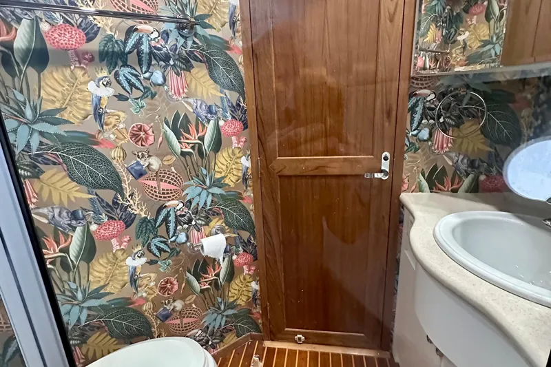Chasing Sunsets Yacht Photos Pics Bathroom of 2000 Pacific Mariner 65 Motoryacht with vibrant tropical wallpaper and wooden door.