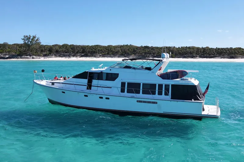 Chasing Sunsets Yacht Photos Pics 2000 Pacific Mariner 65 Motoryacht cruising in clear turquoise waters near a sandy shoreline.