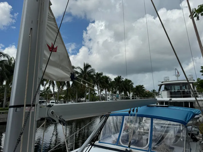 Pura Vida Yacht Photos Pics 2022 Dufour 530 sailboat docked, featuring mast and sail, with palm trees and cloudy sky.