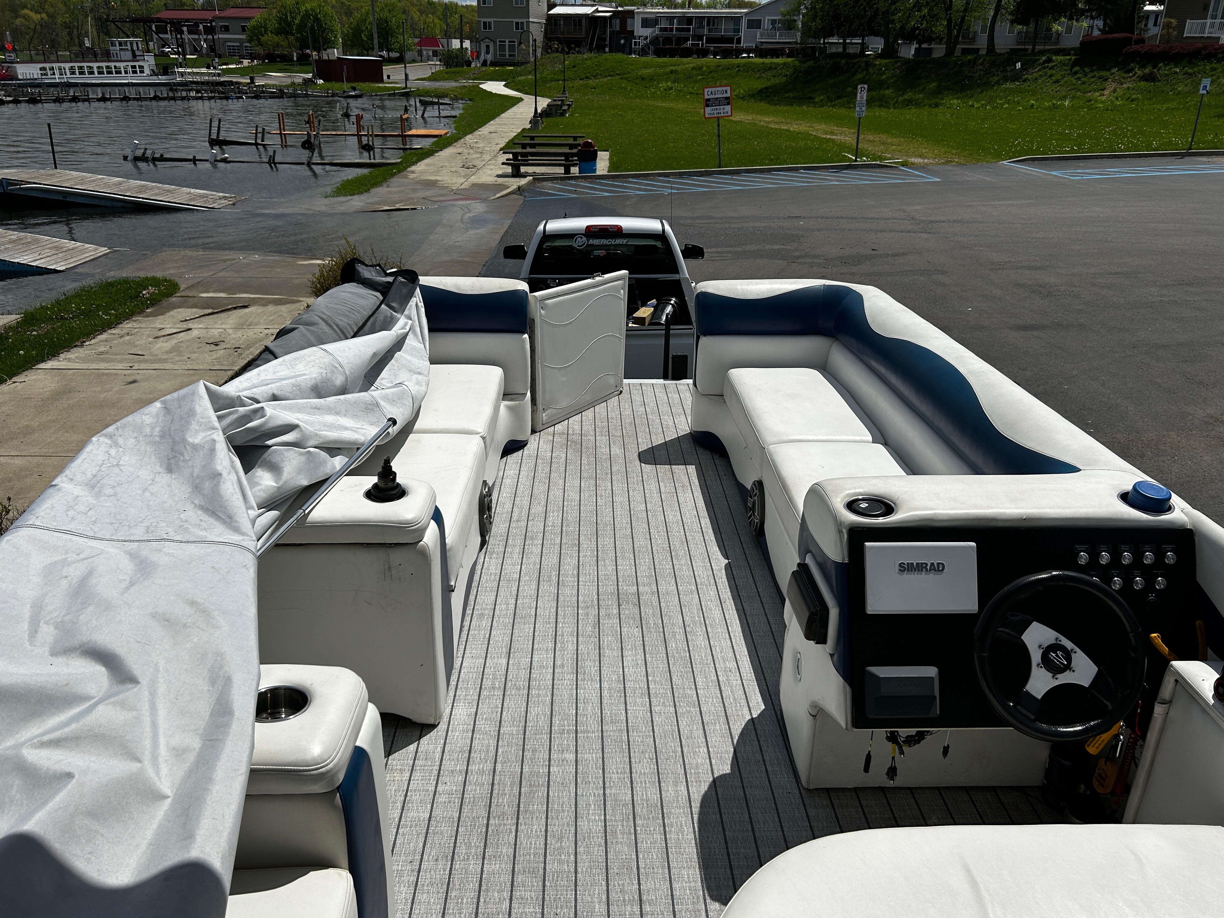 Pontoon boat interior with white seating, docked near a lake, Evolution 26 model, 2005.