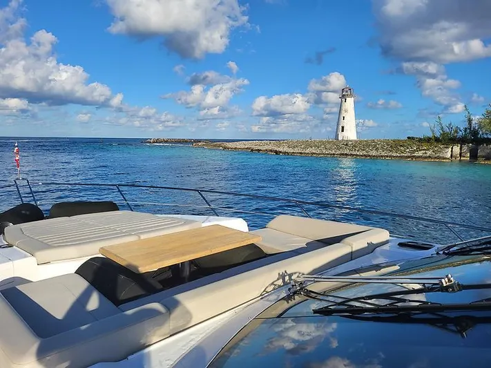  Yacht Photos Pics Sunseeker Predator 74 XPS yacht near a lighthouse, clear blue water, and cloudy sky.