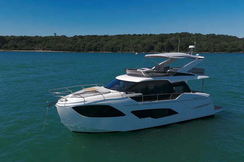 In Stock Yacht Photos Pics 2025 Absolute 47 Fly yacht on serene blue water, with lush green shoreline.