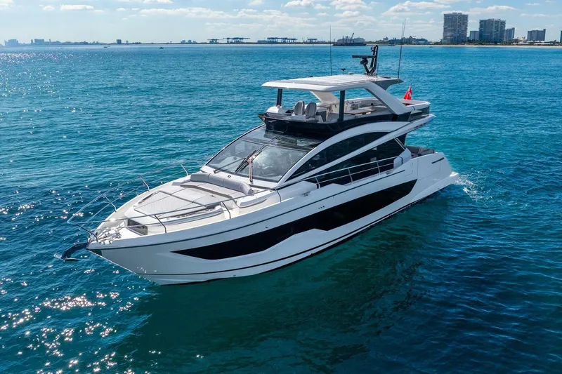  Yacht Photos Pics Luxurious 2025 Pearl 63 yacht cruising on clear blue ocean near city skyline.