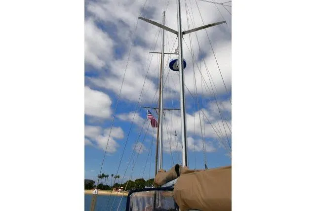 Avenir Yacht Photos Pics Mason 63 sailboat mast with American flag, clear sky, and palm trees in the background.