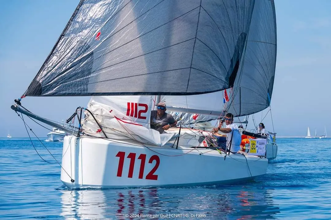 2024 Mini 650 sailboat racing on calm blue waters, numbered 1112.
