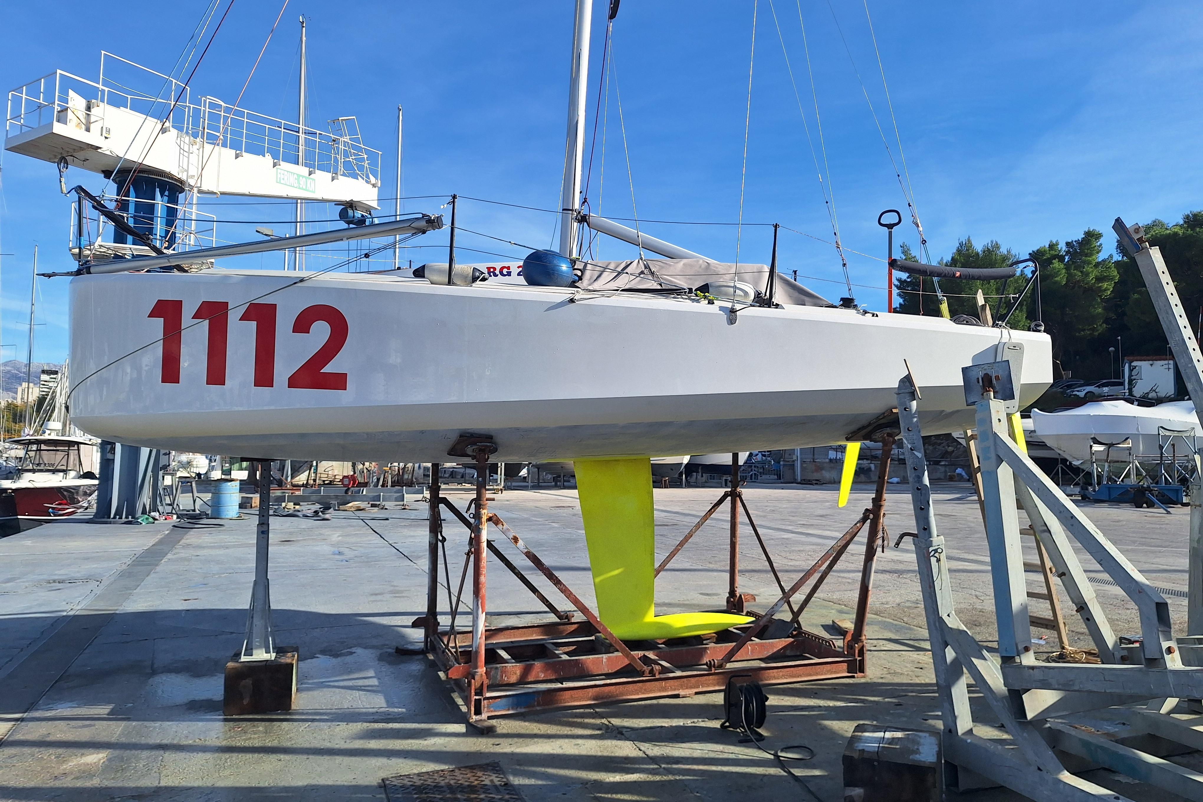 2024 Mini 650 sailboat on dry dock, displaying number 1112, with vibrant yellow keel.