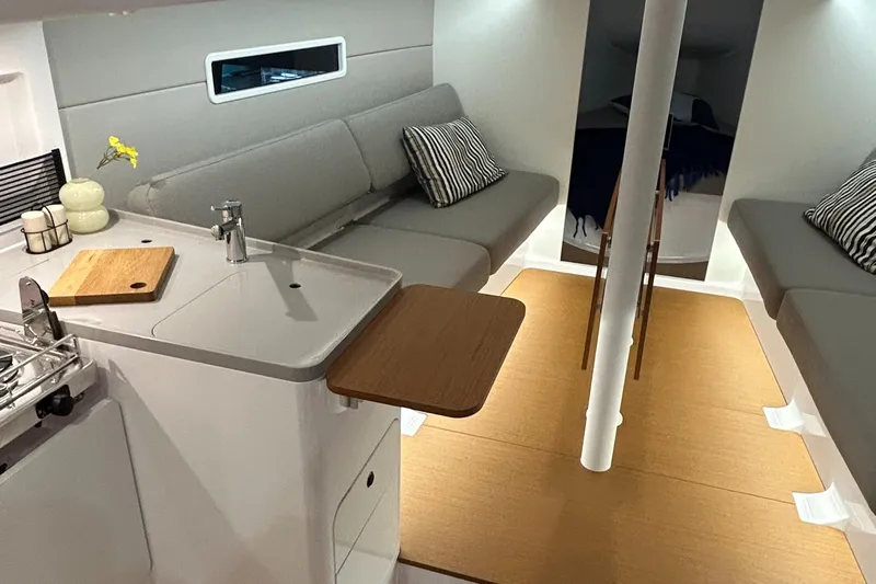  Yacht Photos Pics Interior of 2025 Beneteau First 30 sailboat with modern seating and compact kitchen area.