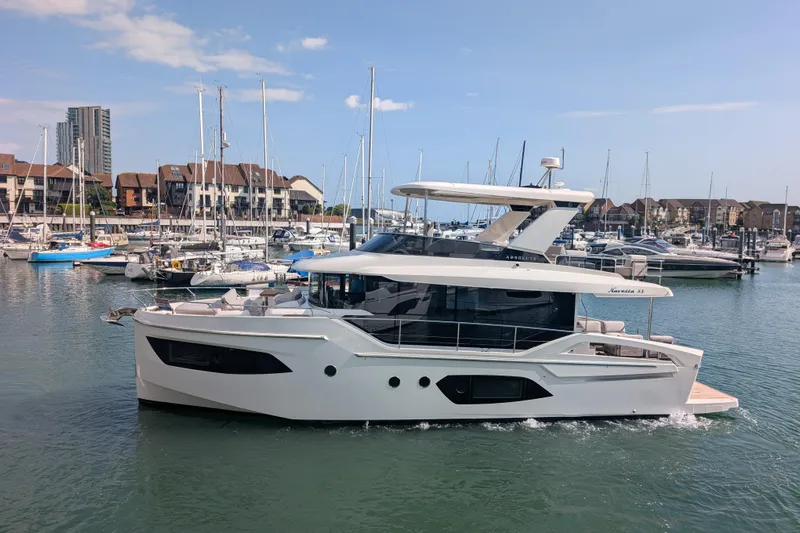 In Stock Yacht Photos Pics 2025 Absolute Navetta 53 yacht cruising in a marina with sailboats and buildings in the background.