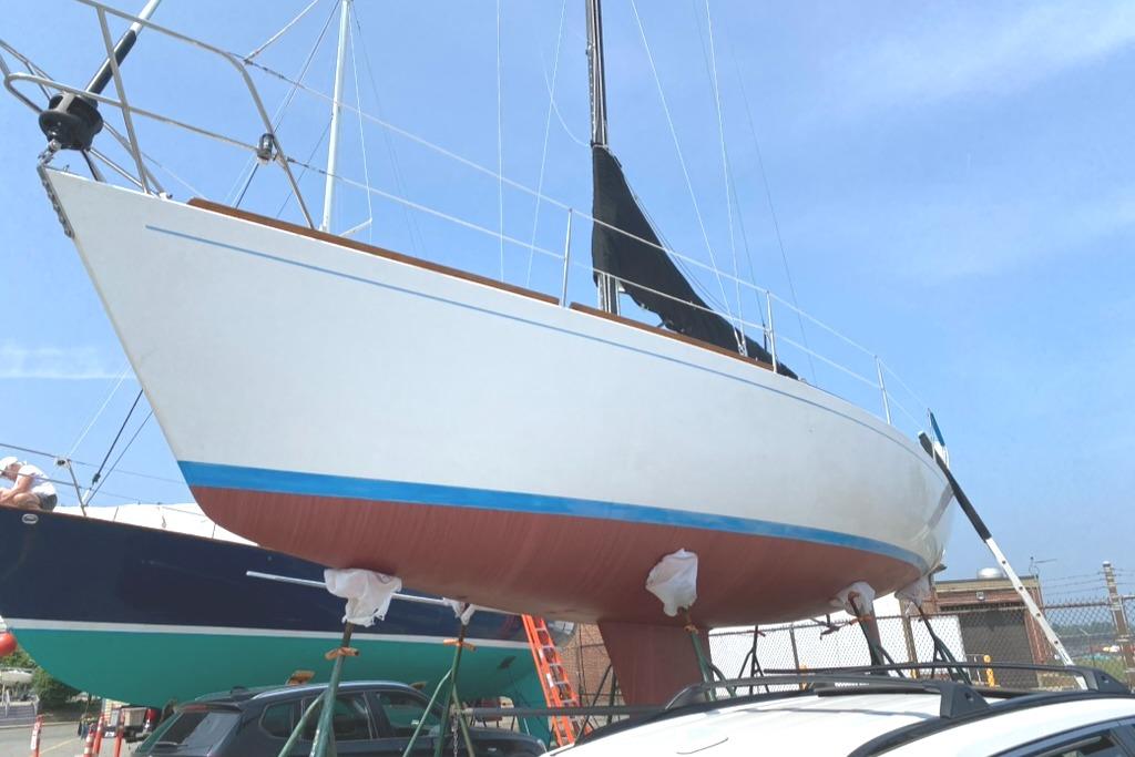 1986 Express 37 sailboat on dry dock, white hull with blue stripe, clear sky background.