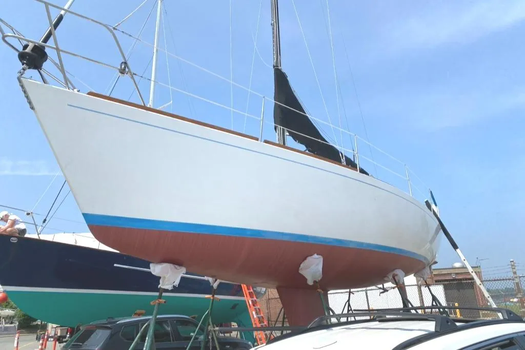 1986 Express 37 sailboat on dry dock, white hull with blue stripe, clear sky background.