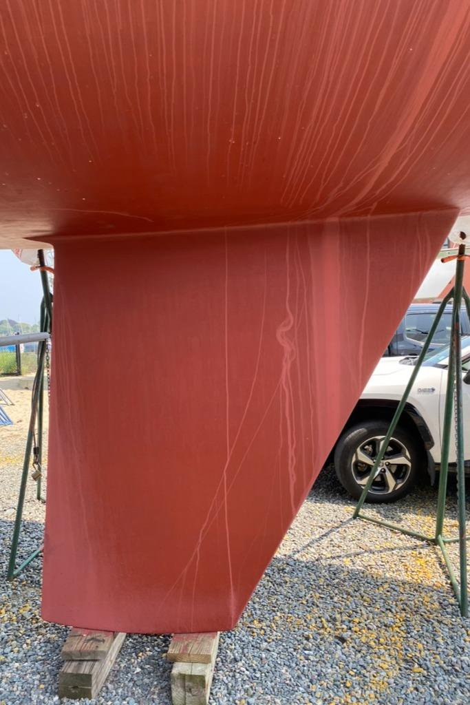 Red hull of 1986 Express 37 sailboat on stands, gravel ground.