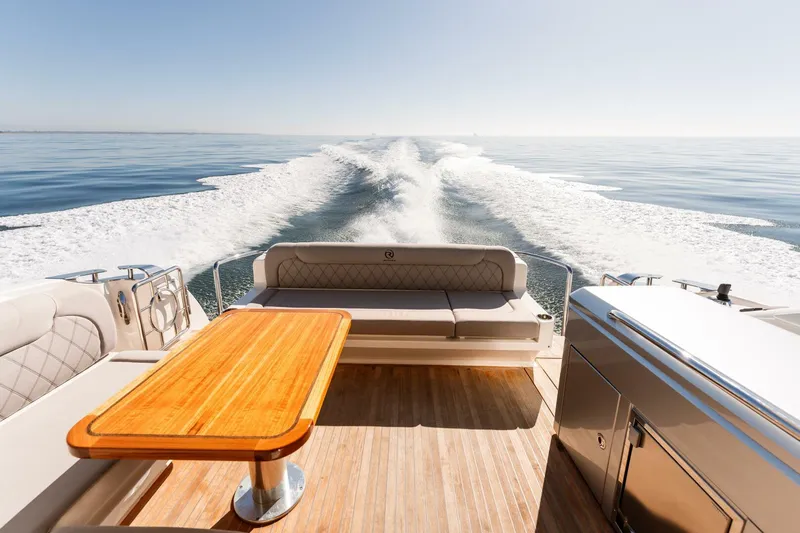 Ventures64 Yacht Photos Pics 2022 Riviera 4800 Sport Yacht cruising on open water, featuring elegant deck seating and table.